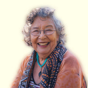 Smiling elderly woman wearing glasses and a patterned scarf on a light background